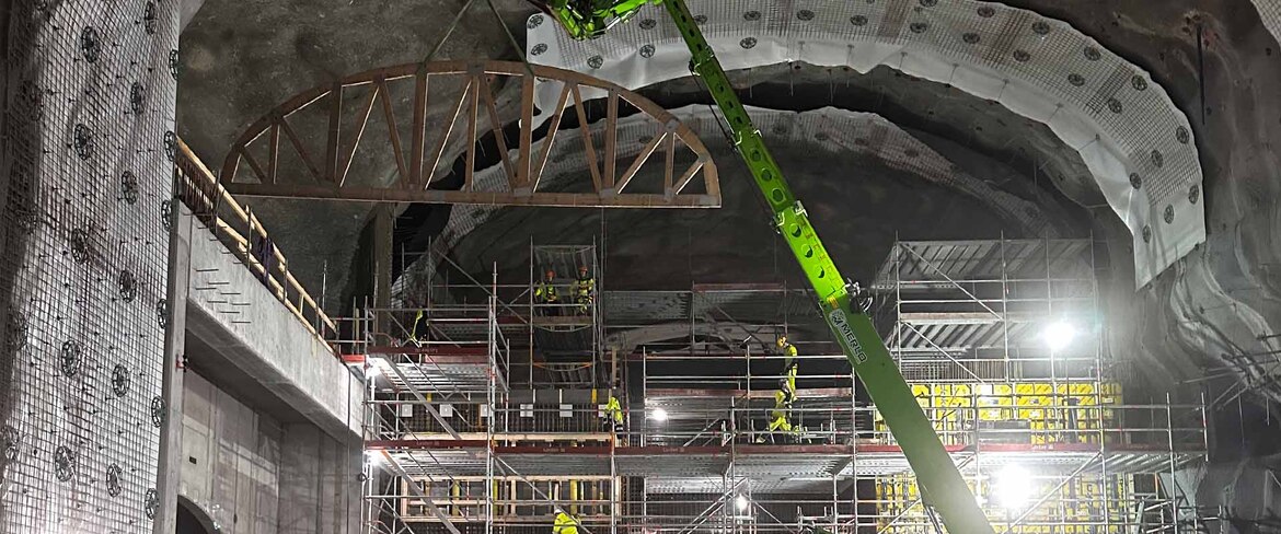En stor grön lift som lyfter en specialbyggt träkonstruktion i ett stort byggprojekt.