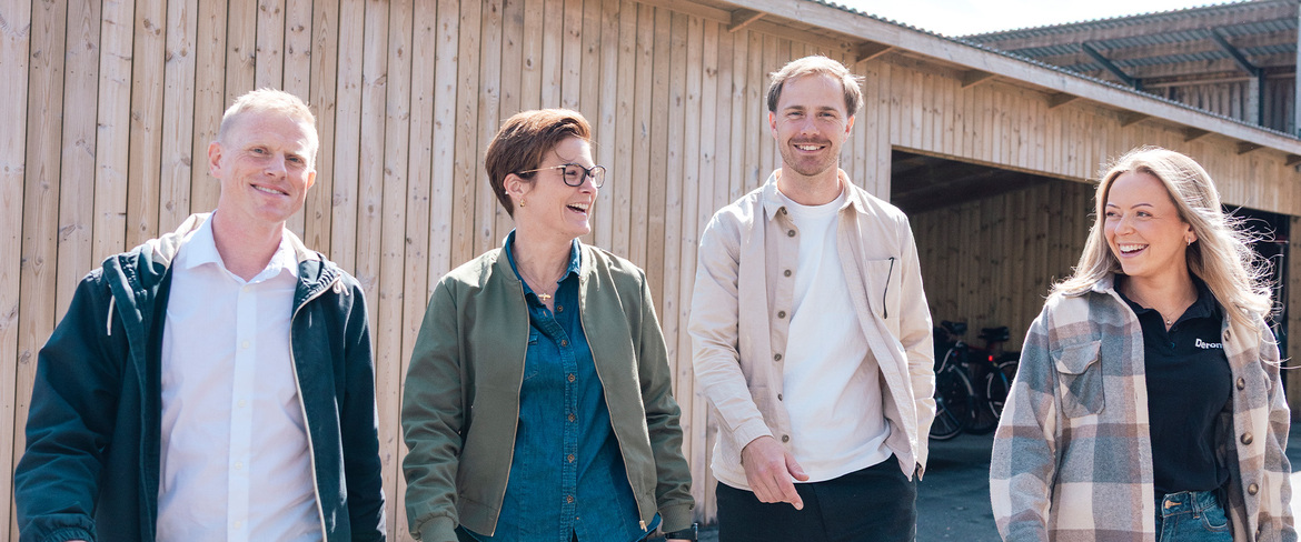 fyra glada kollegor går tillsammans i en utomhusmiljö med träpanel i bakgrunden. 
