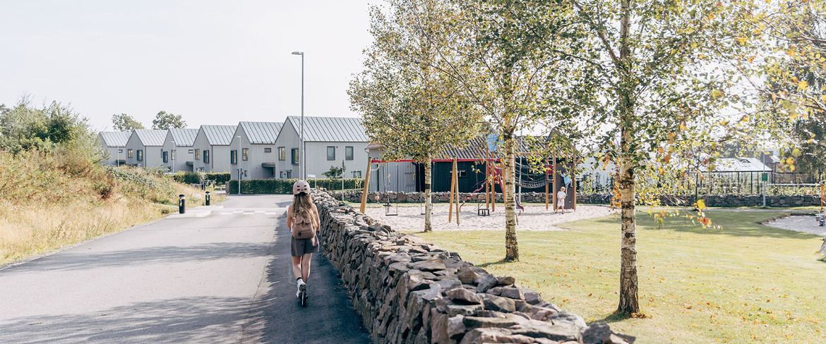 Ett barn cyklar på en sparkcykel i ett grönskande bostadsområde. 