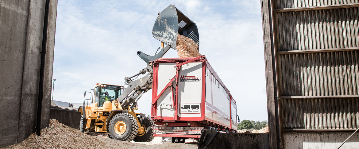 En traktor lastar på med biobränsle i en lastbil. 